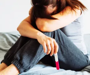 Femme assise avec un test de grossesse dans la main, exprimant stress, culpabilité et difficultés liées à la maternité