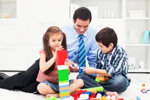 Un homme en costume joue aux Lego avec ses enfants, symbolisant l’équilibre entre responsabilités professionnelles et vie personnelle.