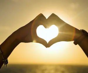 Mains formant un cœur face au coucher du soleil, symbole de reconstruction et de reconnexion corporelle et émotionnelle