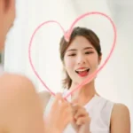 Femme souriante traçant un cœur sur un miroir embué, symbole de reconstruction progressive et de confiance retrouvée
