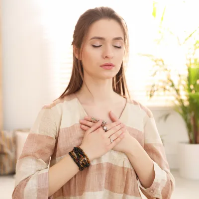 Femme en méditation, mains sur le cœur, représentant la connexion intérieure et la transformation énergétique grâce au ThetaHealing® avec Nadège Augereau.