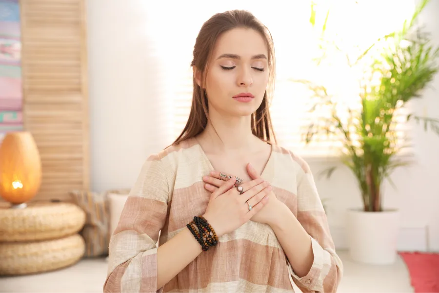 Femme en méditation, mains sur le cœur, représentant la connexion intérieure et la transformation énergétique grâce au ThetaHealing® avec Nadège Augereau.