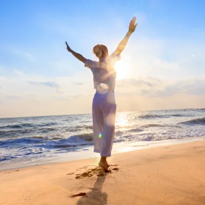 Femme levant les bras au soleil couchant sur une plage, symbole de libération émotionnelle et de bienêtre grâce au ThetaHealing
