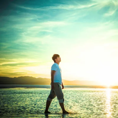 Jeune homme sur la plage réfléchissant à sa vie avec positivité après une séance neuroénergétique avec Nadège Augereau
