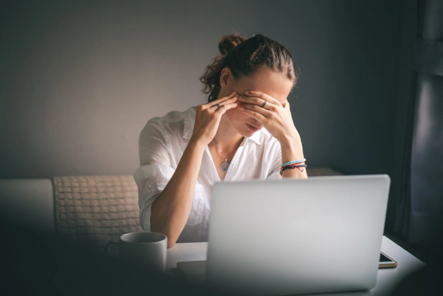 Femme assise devant son ordinateur, submergée par le stress, le doute de soi et le manque de confiance en elle.