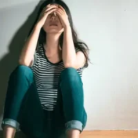 Femme assise au sol les mains sur la tête, submergée par ses pensées