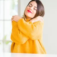Femme souriante dans un geste d’autocâlin, illustrant la réconciliation avec soimême